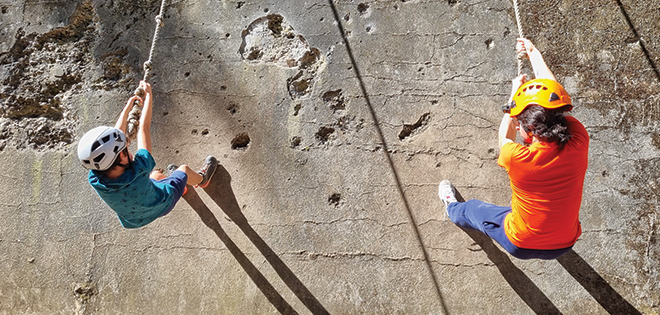 Deux jeunes descendent en rappel un mur. Ils sont sécurisés. 